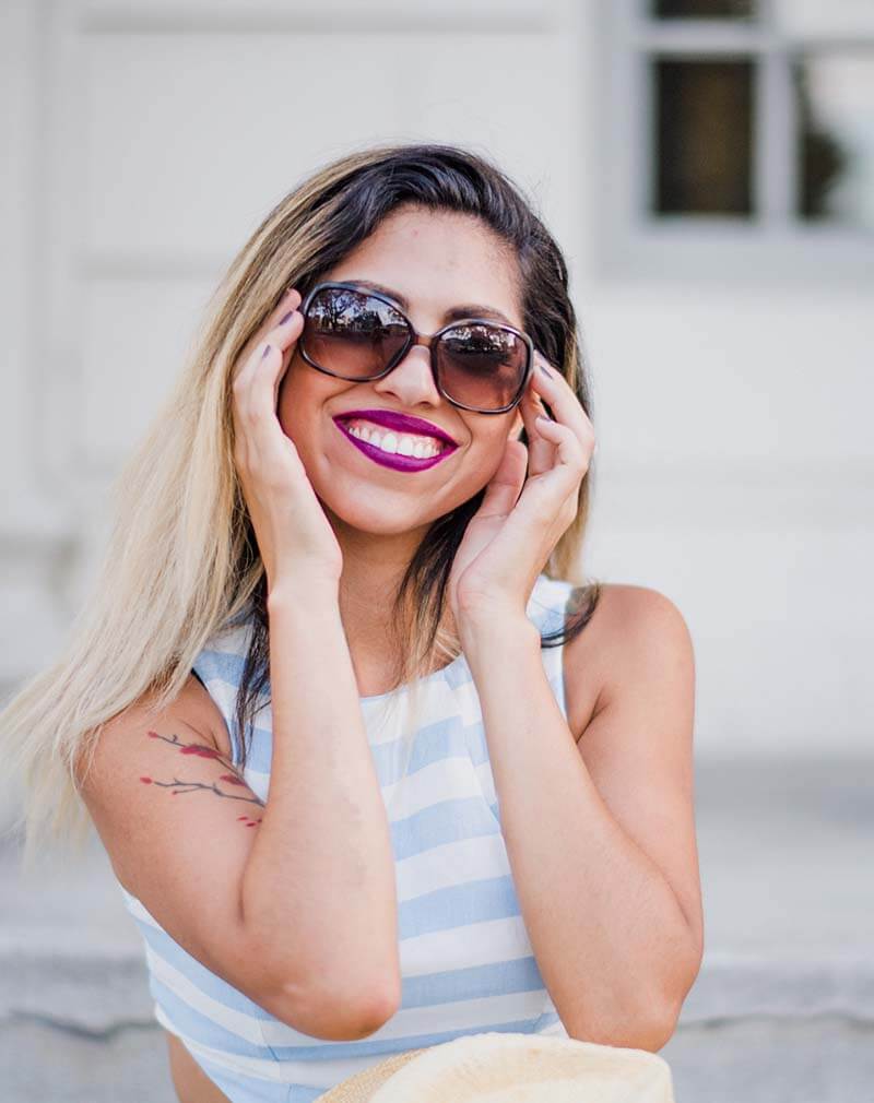 Blonde-girl-holding-up-a-pair-of-black-sunglasses-and-smiling