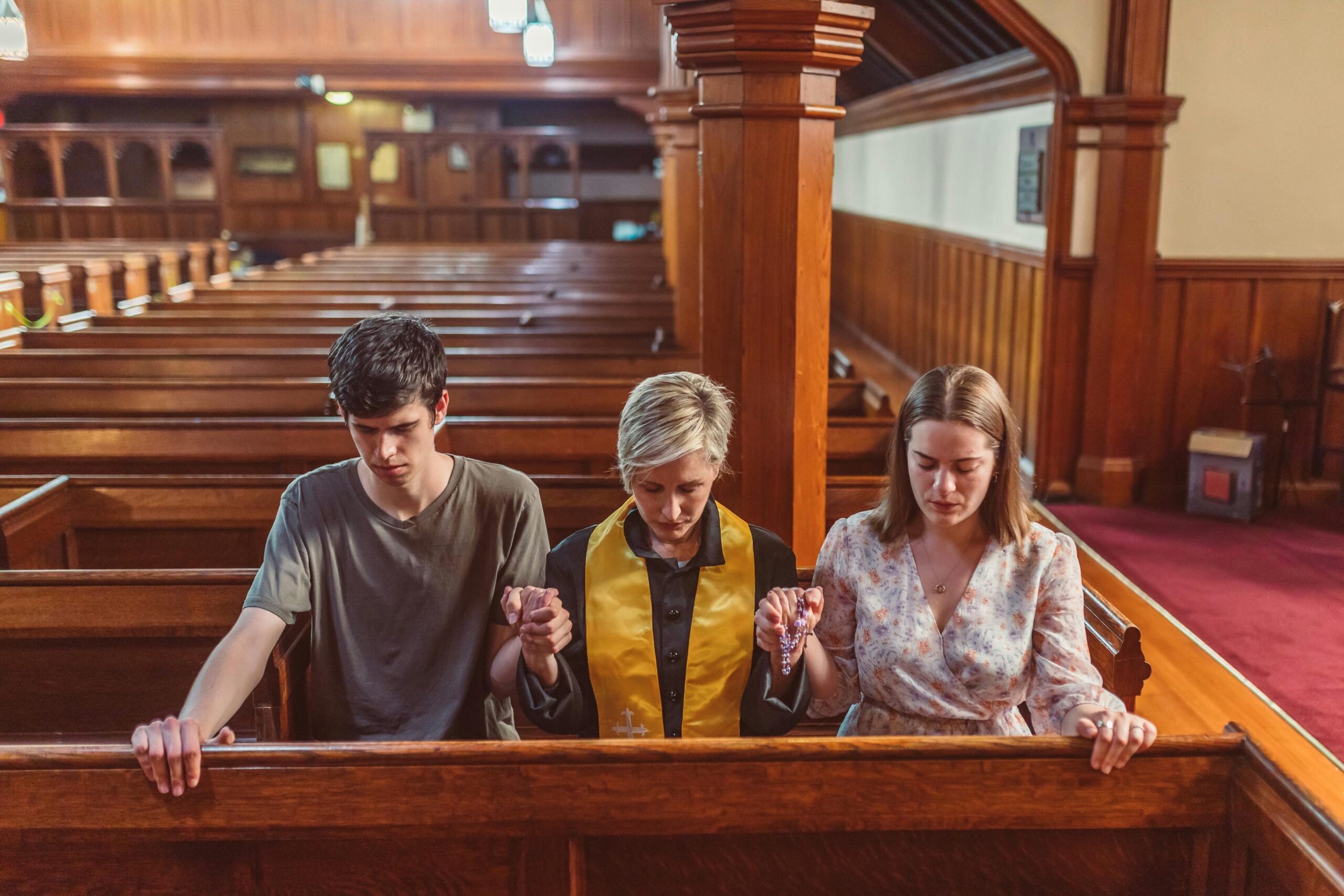 Three-people-sitting-in-church-pews-praying-silently-together-with-their-heads-bowed